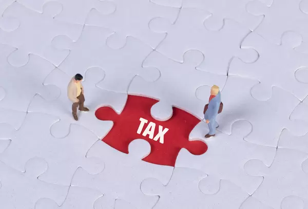 Two miniature man looking at a missing puzzle piece with Tax text