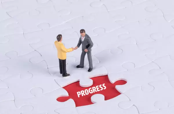 Two miniature man shaking hands and a missing puzzle piece with Progress text