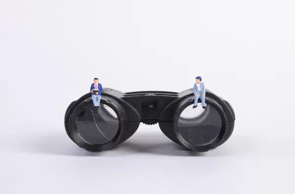 Two miniature man sitting on binoculars
