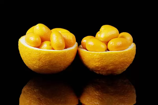 Two orange halves full with kumquats fruits, black background