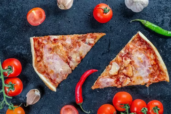 Two slices of homemade pizza on a black background with vegetables. Top view