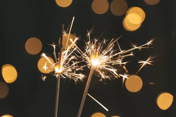 Two sparklers are lit on a blurred background of a glowing garland