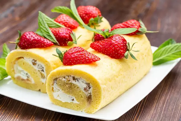 Two sponge rolls with cottage cheese cream and raisins decorated with strawberries and mint
