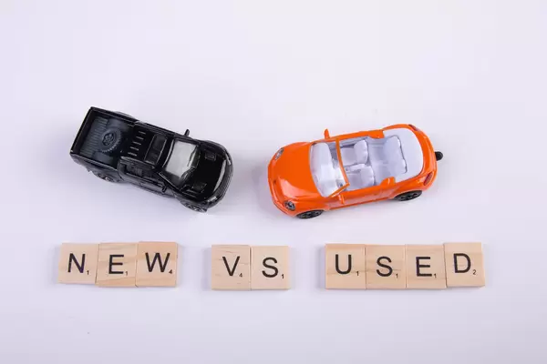 Two toy cars with New vs Used text on wooden blocks