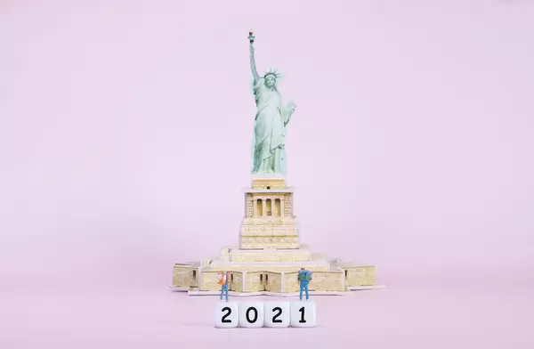 Two travelers standing on blocks with 2021 text in front of Statue Of Liberty