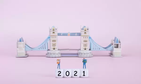 Two travelers standing on blocks with 2021 text in front of Tower Bridge