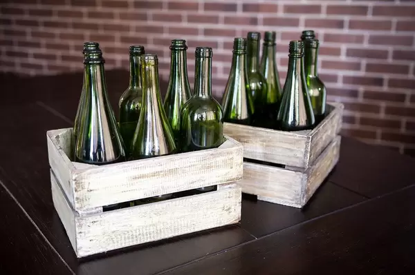 Two wooden boxes of different shaped green wine bottles on rustic background