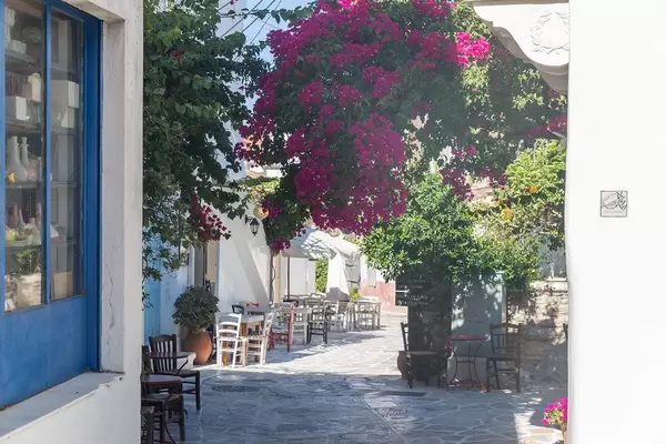 Typical Greek alley on the island Naxos with white-blue buildings, bougainvillea plants, restaurant tables