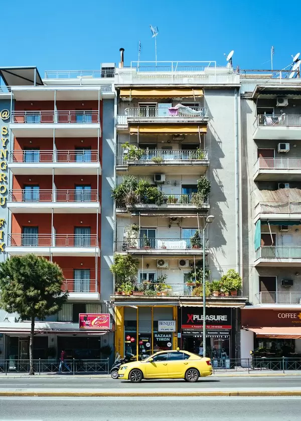 Typisches griechisches Wohnhaus mit grünen Balkonen und gelben Taxi vor der Tür, in Athen (Griechenland)