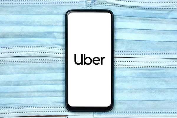 Uber company logo on smartphone screen over the face masks. Global company during coronavirus crisis