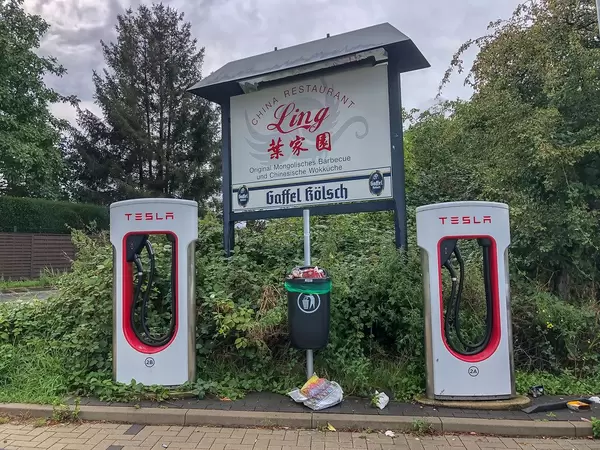 Überfüllter Mülleimer und Umweltverschmutzung zwischen zwei Tesla Supercharging E-Ladesäulen für Elektroautos