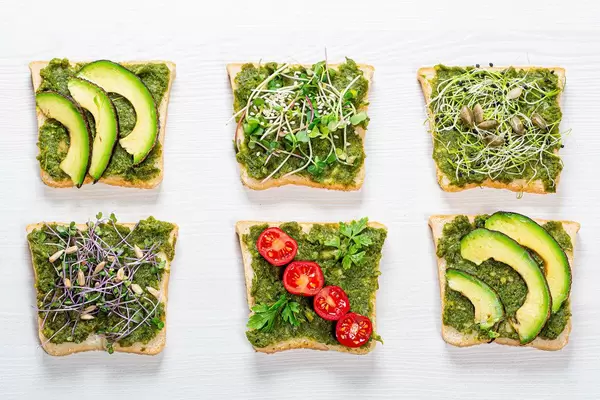 Übersicht von diversen Sandwiches mit Kräutern, Mikrogrün, Gemüse und Samen auf weißem Holzhintergrund