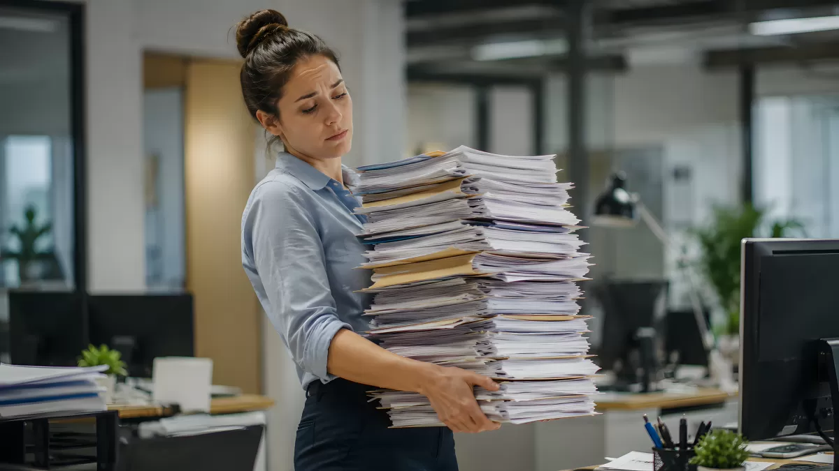 Überarbeitete Büroangestellte trägt riesigen Papierstapel