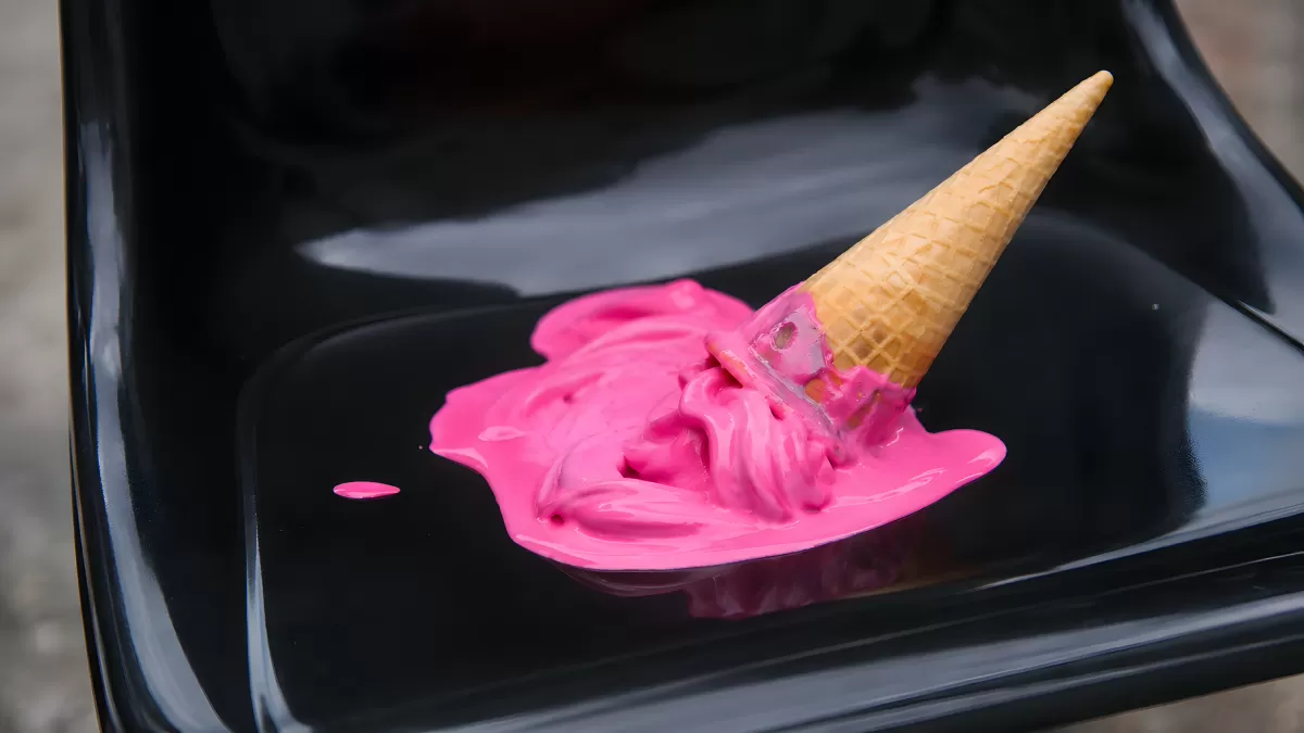 Umgefallene Eistüte mit rosa Eis auf schwarzem Stuhl