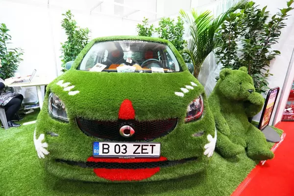 Ums Thema Nachhaltigkeit bei Automesse in Rumänien: Mercedes Smart mit Kunstrasen bedeckt mit grünem Bär und Pflanzen als Deko