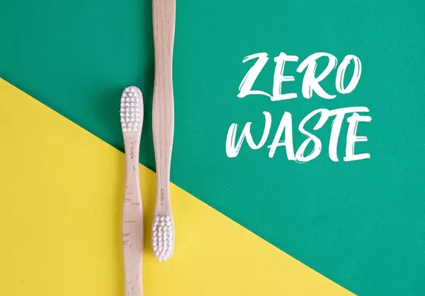 Umweltfreundliche Holzzahnbürste auf grünem und gelben Untergrund und dem Text "Zero Waste"