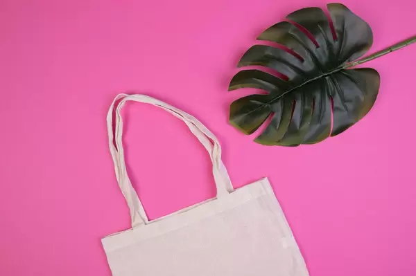 Umweltfreundliche, wiederverwendbare Einkaufstasche aus Baumwolle neben Blatt vor pink