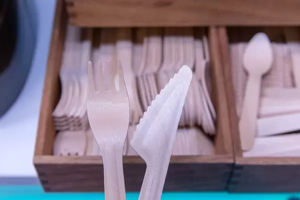 Umweltfreundliches Einwegbesteck wie Messer und Gabel aus Holz vor Kiste mit weiterem Besteck