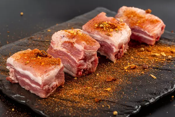 Uncooked pork ribs with ground spices on a dark background