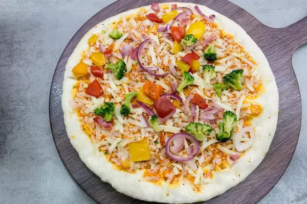 Ungebackene vegetarische Pizza auf einem Holzschneidebrett