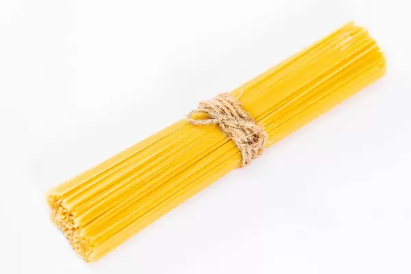 Ungekochte Spaghetti mit Bastschnur gebunden vor weißem Hintergrund
