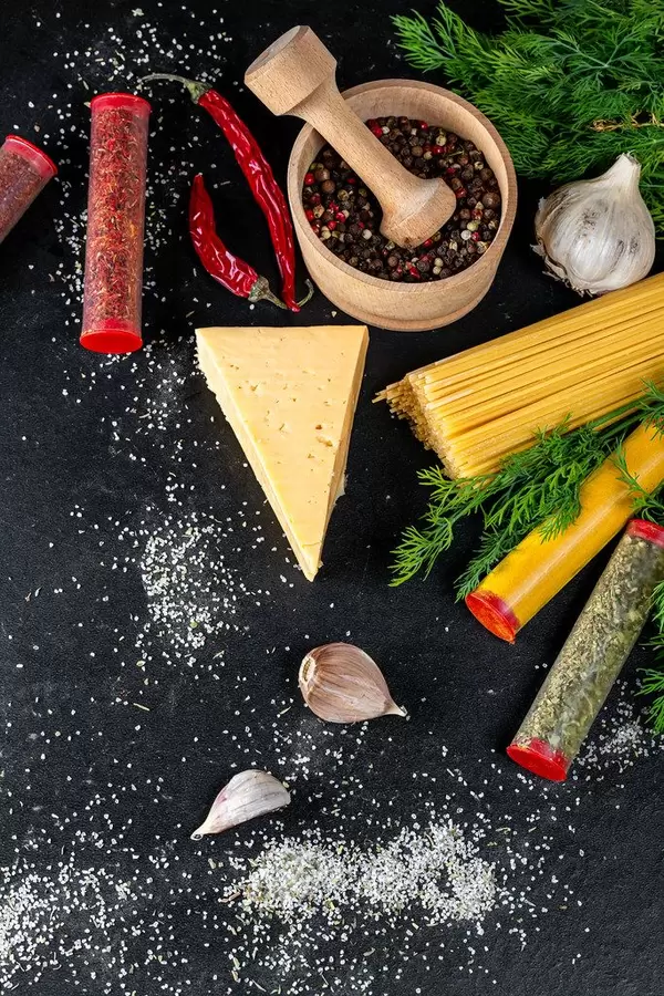 Ungekochte Spaghetti mit Gewürztuben und Pferfferkörner im Mörser, auf einem schwarzen Hintergrund