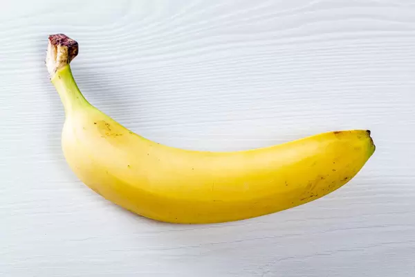 Ungeschälte, ganze Banane liegt auf weißem Holztisch