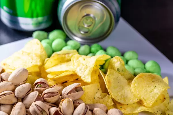 Ungeschälte Pistaziennüsse, Wasabi und Kartoffelchips vor Bierdosen