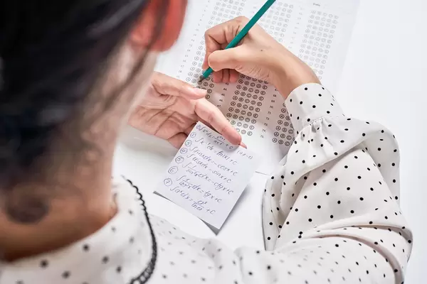 University student holds pencil doing math test exam and cheats with answers piece of paper in hand