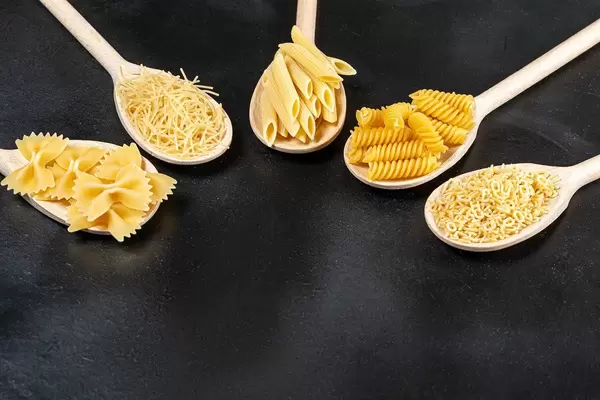 Unterschiedliche Formen von Pasta in Holzlöffeln auf schwarzem Hintergrund