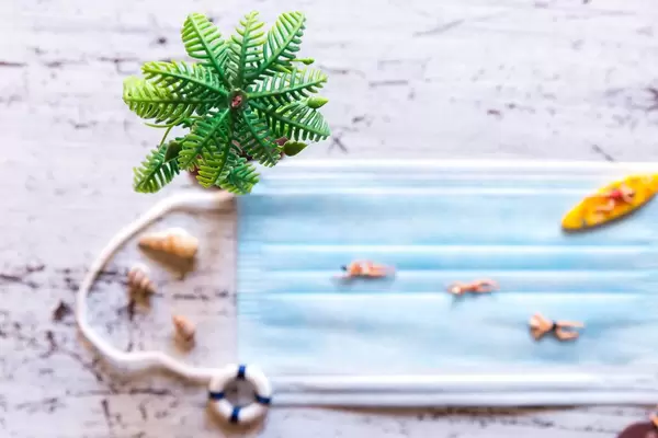 Urlaub am Strand in Zeiten von Corona: Miniatur-Figuren schwimmen und surfen auf Mundschutz