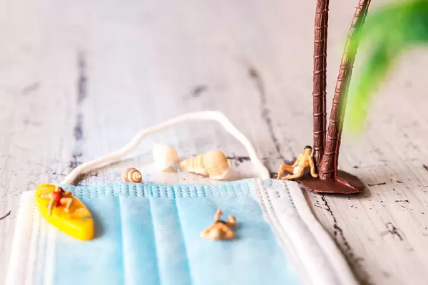 Urlaub trotz Corona. Nahaufnahme: Miniaturfiguren, die einen Mundschutz als Strand benutzen