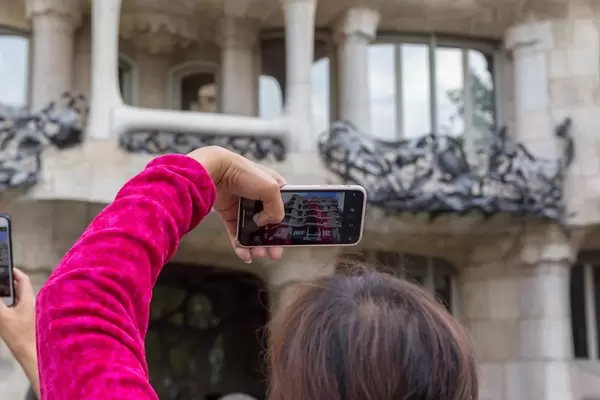 Urlauberin fotografiert mit ihrem Smartphone das Unesco Weltkulturerbe und Meisterwerk von Antoni Gaudi "Casa Milà"