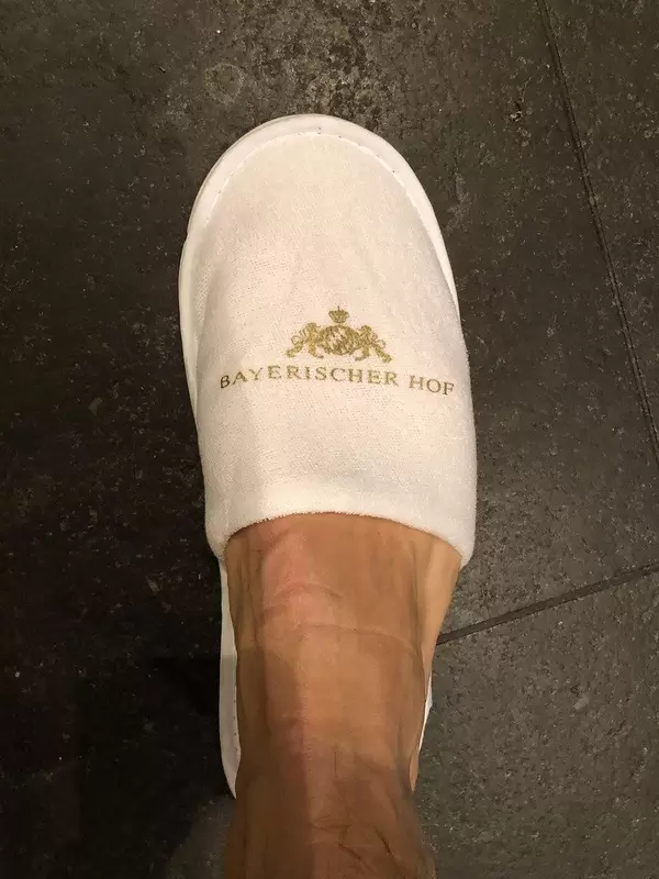 Urlaubsgast trägt weiße Hotelschlappen mit der Aufschrift "Bayerischer Hof"