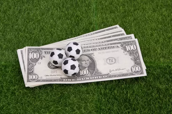 US dollar banknotes with soccer balls on green grass