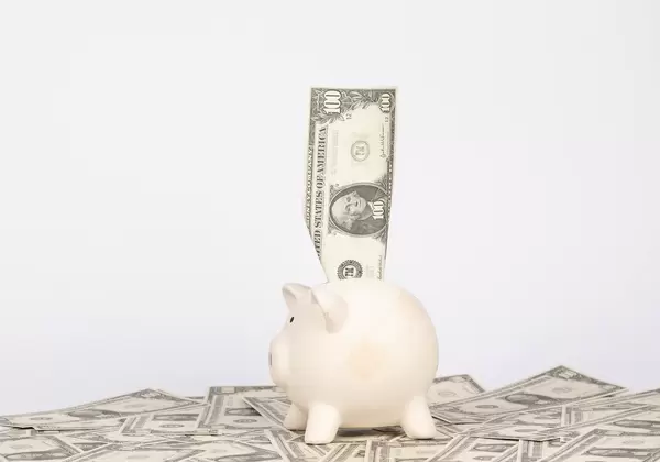 US-Dollar Note steckt in Sparschwein das auf Banknoten liegt vor weißem Hintergrund