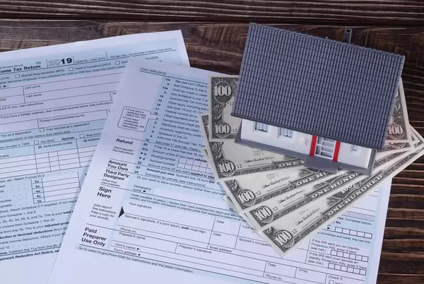 US tax forms and a miniature house symbolizing the savings or costs of owning real estate