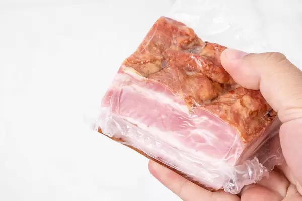 Vacuumed piece of bacon in the hand above white background (Flip 2019)