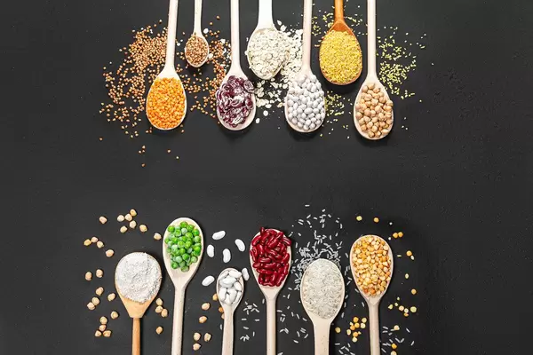Various legumes, peas, buckwheat, rice, chickpeas, lentils, oat flakes, oat bran in wooden spoon on black background. Top view (Flip 2019)