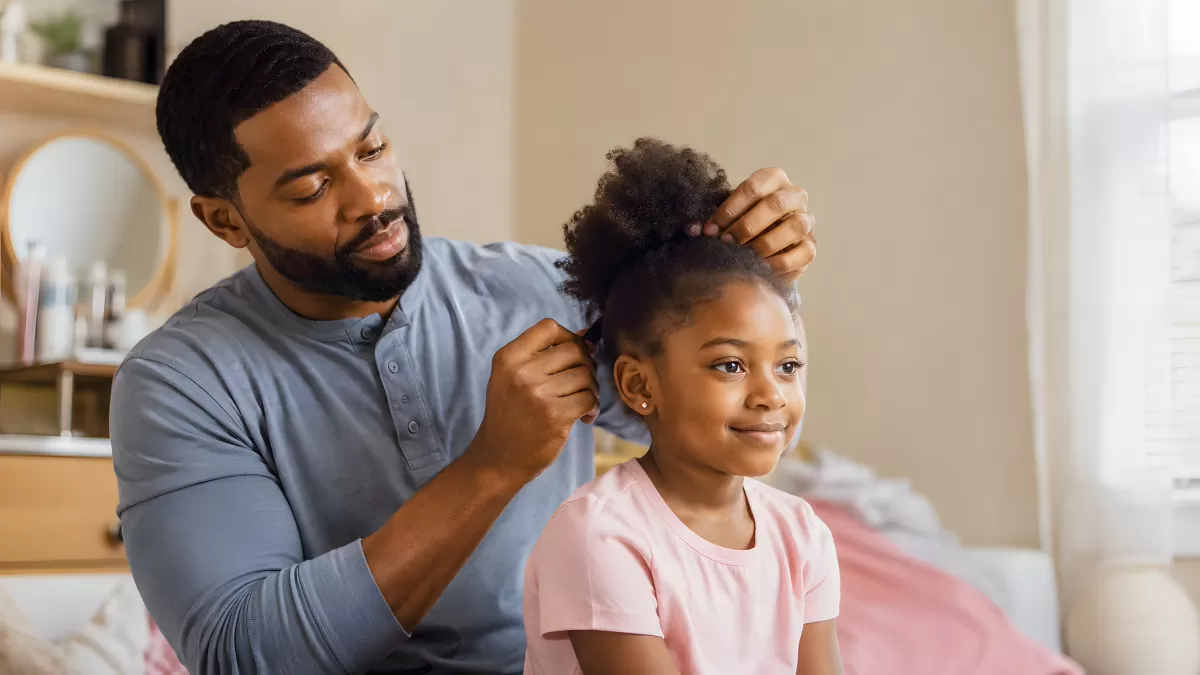 Vater frisiert seiner Tochter die Haare im Kinderzimmer