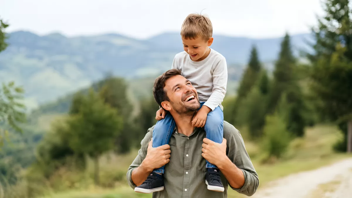 Vater trägt lachenden Sohn auf den Schultern in der Natur