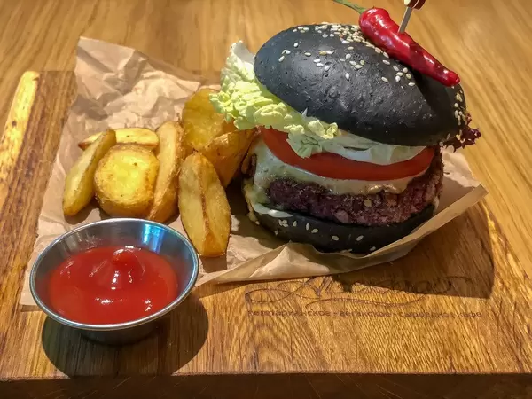 Veg Kuro Burger beim Avocado Cafe: Frikadelle aus Linsen und Müsli, mit Holzkohle geschwärztes Brötchen, Erdnusssauce, Tomate, Essiggurke, Kopfsalat, Chili