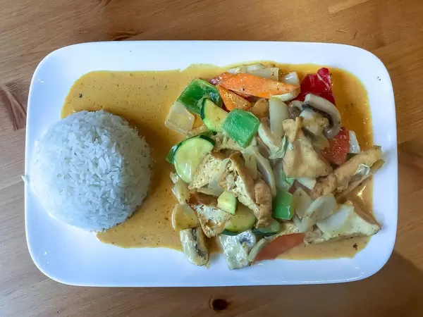 Vegan Asia Meal - Red thai curry with tofu, zucchini, mushrooms, bellpepper, carrots and rice on a plate on wooden table