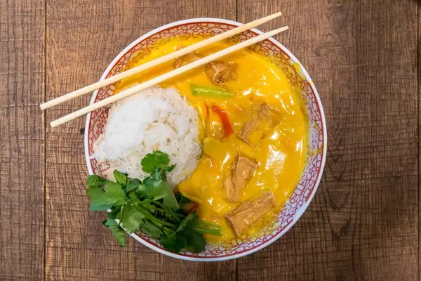 Vegan asian food at coa restaurant: yellow coconut curry with tofu, sweet pepper, mushrooms, sweet potatoes, rice, spinach, in a bowl with chopsticks