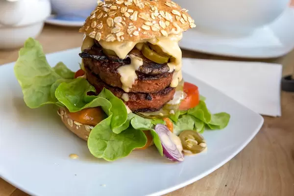 Vegan Beyond Meat Burger with Beyond Meat Patty, Ketchup Special, salad, gherkins, tomato, red onions and Portobello mushroom bacon on white plate