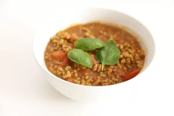 Vegan Bolognese made of sunflower seeds, prepared with tomato sauce and served in a white bowl with basil leaves