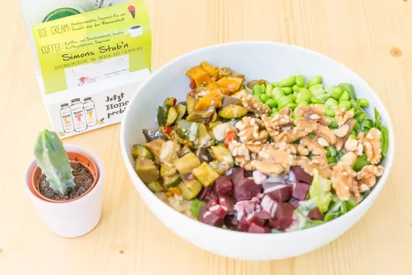 Vegan Bowl with grilled vegetables, beetroot, edamame, walnuts, lettuce, rice and soy-sesame dressing in white bowl