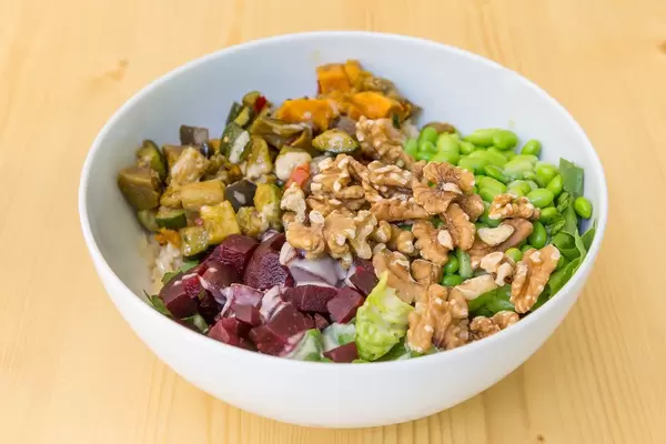 Vegan Bowl with grilled vegetables, rice, walnuts and edamame in a white bowl on a wooden table
