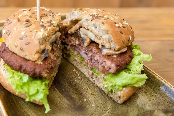 Vegan Burger and meat substitute by Moving Mountain  at "Hans im Glück", cut in half, with juicy patty, green salad, mushrooms and wholemeal bread