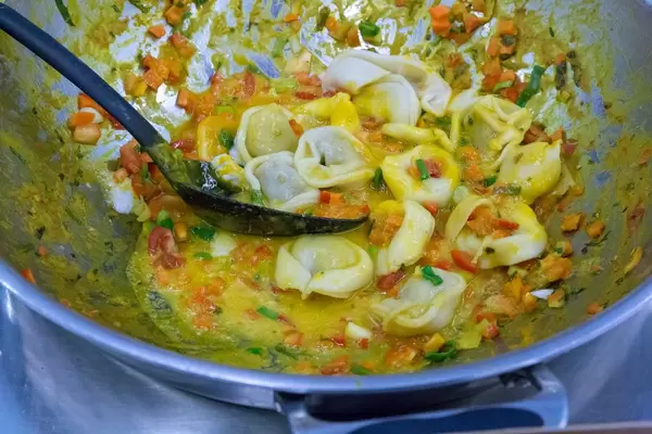 Vegan organic pasta cappelletti with pumpkin-apple filling are prepared in a sauce with carrots and peppers
